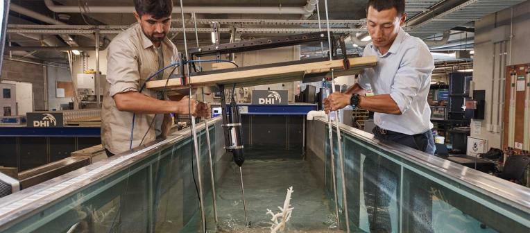 Researchers hold a piece of equipment in a tank of water in a UQ hydraulics lab