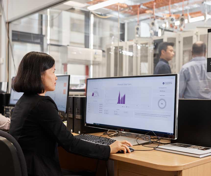 UQ expert monitors graphs on a computer while colleagues investigate equipment in a neighbouring room